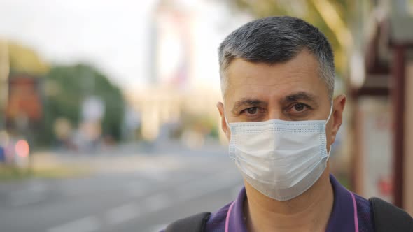 Portrait of a Man in a Medical Mask Waiting for a Bus at a Bus Stop alt