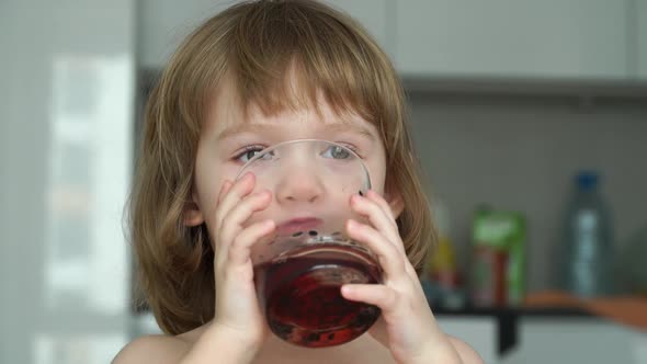 Little Girl Drinks Cherry Juice From Glass Looks at Camera Laughs and Smiles alt