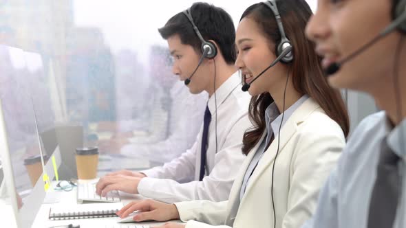 Asian woman smiling at camera while working with team in call center office