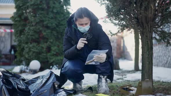 Front View Portrait of Concentrated Smart Criminologist Examining Murder Weapon with Magnifying alt