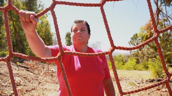 Determined woman climbing a net during obstacle course alt