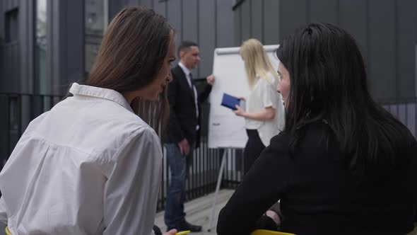 Young Caucasian Women Gossiping As Blurred Coworkers Talking at Background at Whiteboard alt