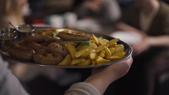 Live Camera Follows Tray with Grilled Potato and Sausages in Waiter Hands Walking to Table with alt