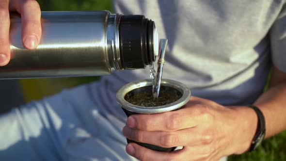 Man Pouring Hot Water Into Yerba Mate Drink From Vacuum Flask. - close up alt