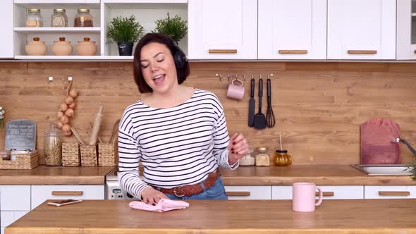 The woman is cleaning the kitchen and dancing. She does housework in a good mood, listens to music alt