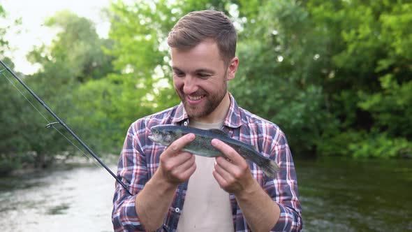 Fisherman Rests on the River and Catches Trout Smiles and Shows the Fish in the Camera alt