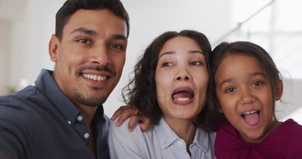 Happy hispanic parents and daughter embracing making funny faces in living room alt