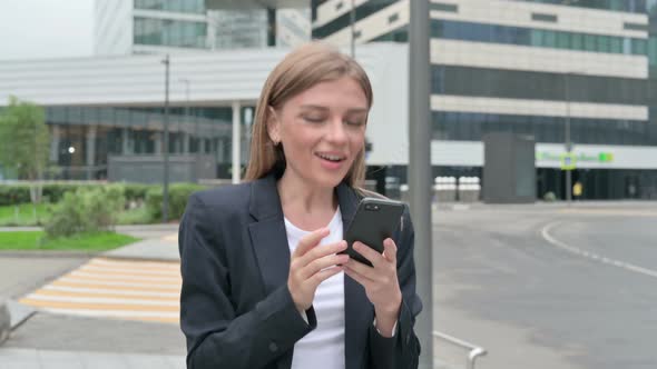 Young Businesswoman Celebrating on Smartphone While Walking on the Street alt