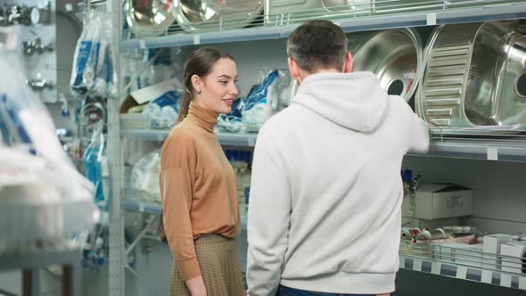 Young Confident Woman Discussing Purchase of New Sink in Hardware Store with Man alt