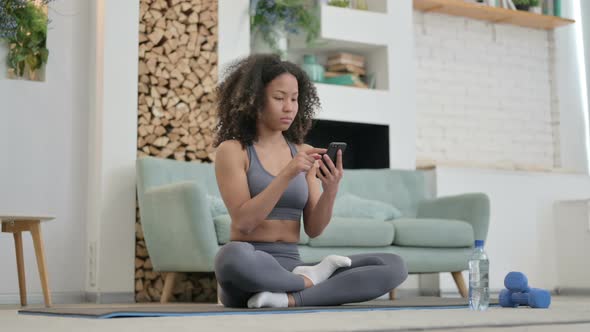 Young African Woman Using Smartphone on Yoga Mat at Home alt