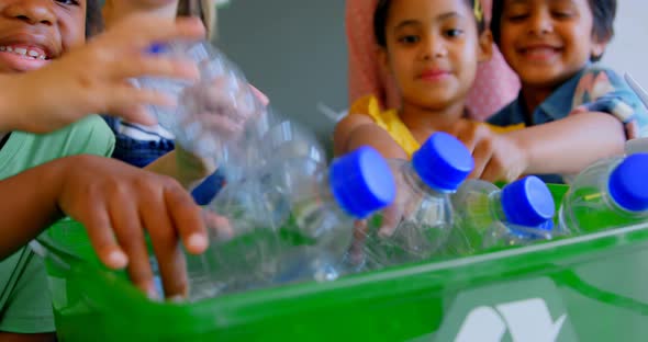 Schoolkids putting bottles in recycle container at desk in classroom 4k alt