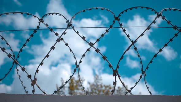 Barbed Wire At The Top Of Fence Against The Blue Sky With Clouds