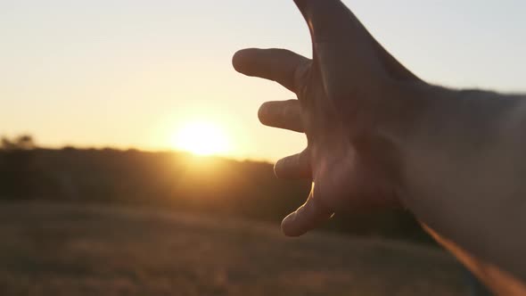 Male Hand Against Sunset. Touch the Sun. Sun Shines Through Fingers. Slow Motion alt