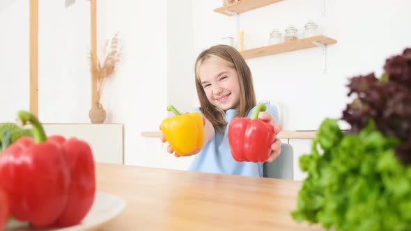 The Little Girl is a Vegetarian She is Smiling and Holding Yellow and Red Peppers alt