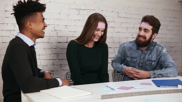 Young Beautiful People in the Office Sitting at the Table Playing Name Game with Sticker Notes alt