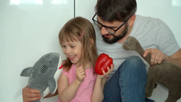 Happy Family Father and Little Daughter Play with Soft Toys and Vegetables in Kitchen