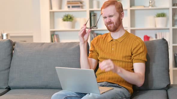 Tired Redhead Man with Headache Working n Laptop at Home alt