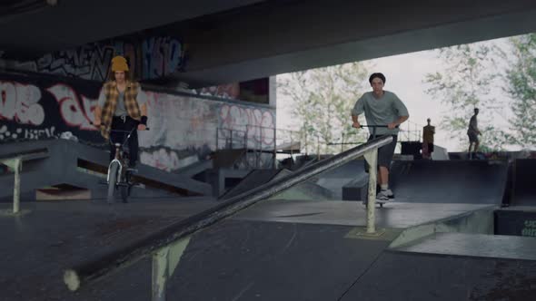 Teenagers Friends Riding Together on Scooter and Bike at City Skatepark alt
