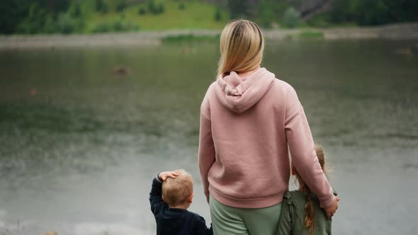 Mother and Little Children Enjoy Calm Lake Standing on Bank alt