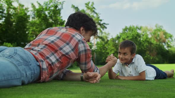 Father and Son Practising Arm Wrestling in Meadow. Boy Winning Competition alt