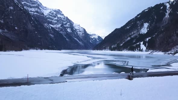 The drone follows a young man who walks on a road of a artifica lake. Later he stops and waves. alt