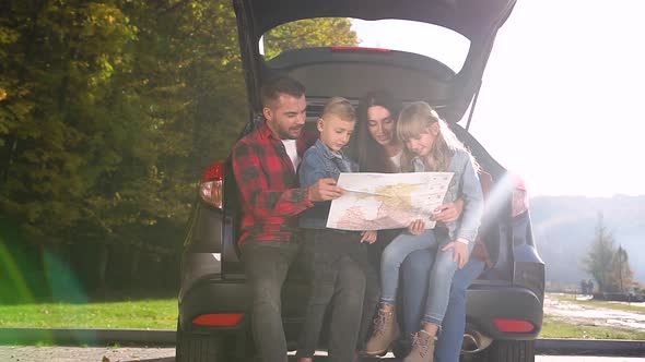 Smiling Dad, Mom and Two Children Sitting in the Trunk and Using Road Map alt