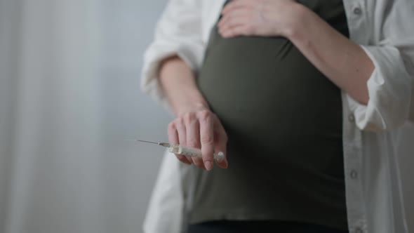 Unrecognizable Pregnant Addicted Woman with Syringe Standing Indoors Touching Belly alt
