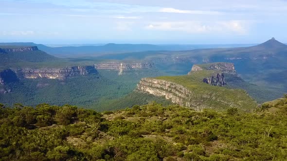 Drone flying over tree lined cliff edge revealing deep valley, mountains and rocky escarpments. Loca alt