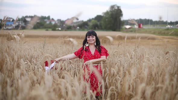 Beautiful Stylish Woman with Dark Hair in a Red Dress in a Field with Hay