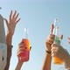 Closeup of Raised Male and Female Hands Holding Bottles with Drinks Dancing Outdoors