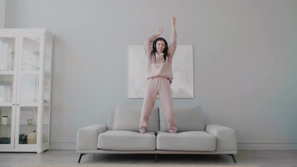 Young Caucasian woman in headphones jumping dancing and singing alone at home.