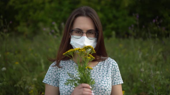 A Young Woman in a Medical Mask Sniffs Flowers and Shakes Her Head Because She Doesnot Smell alt