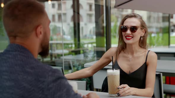 a Couple is Sitting at a Table in an Outdoor Cafe with Cocktails alt