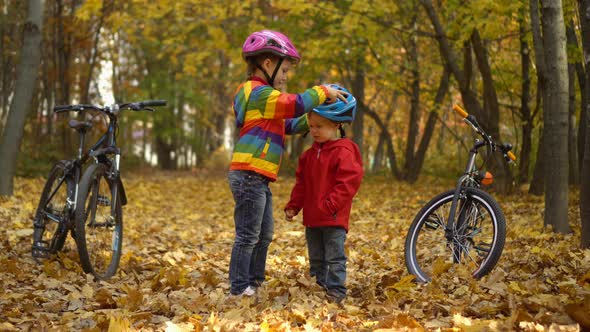 Little kids brother and sister in autumn Park. Older sister helping younger child to put his helmet