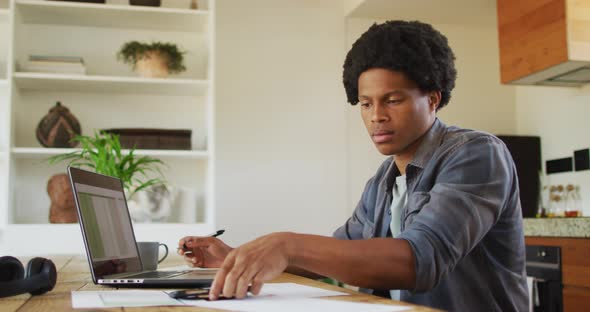 African american man working from home and using laptop and smartphone alt
