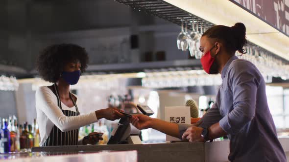 Mixed race man giving african american female cafe worker his credit card in order to pay alt