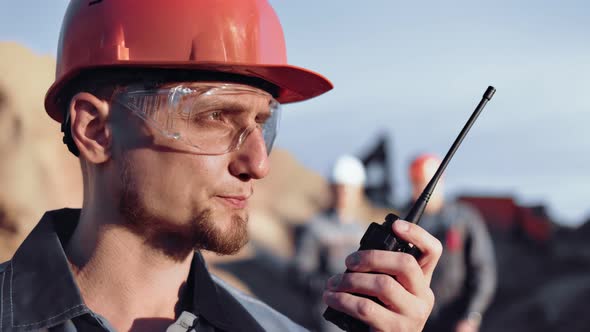 Skilled Male Construction Engineer in Uniform Reporting Using Walkie Talkie During Working Closeup alt