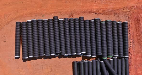 New Black Plastic Pipe with a PVC Seal Stacked in Rows at the Construction Site for a Drain System alt