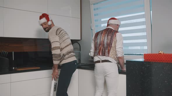 Happy Gay Couple Cleaning the Kitchen with Santa Claus Hats and Having Fun alt