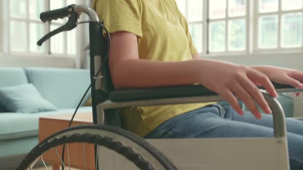 Close Up Of Asian Kid Girl Sitting In A Wheelchair Smiling And Showing Ok Sign In Living Room alt