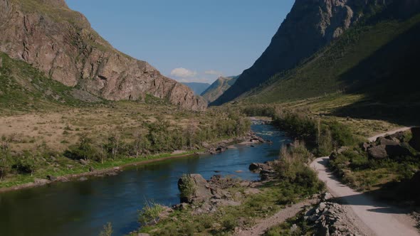 River Chulyshman between green field and mountains with blue clear sky in Altai