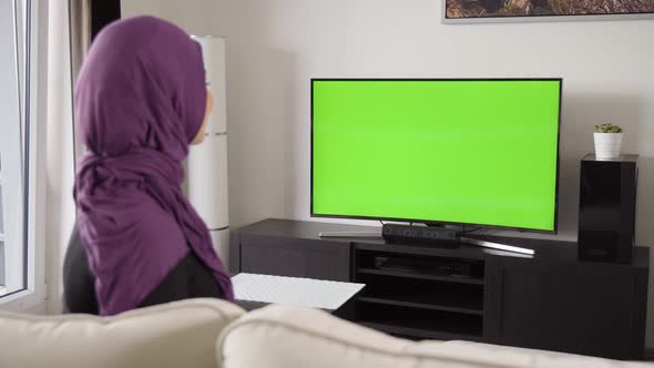 A Muslim Woman Celebrates As She Watches TV with Green Screen in an Apartment  View From Behind alt