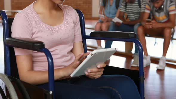 Disabled schoolgirl using digital tablet with classmates in background alt