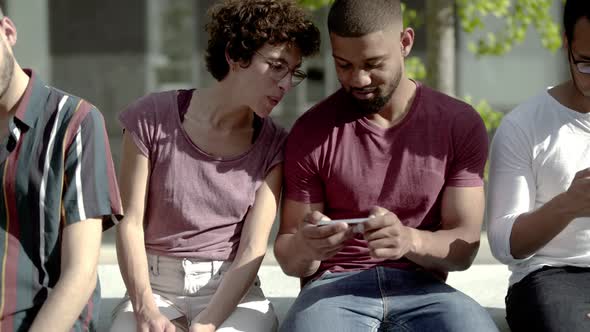 Front View of Two Friends Sitting and Looking at Smartphone  alt