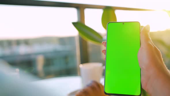 Woman Sitting in a Cafe and Using Smartphone with Green Mockup Screen in Vertical Mode alt