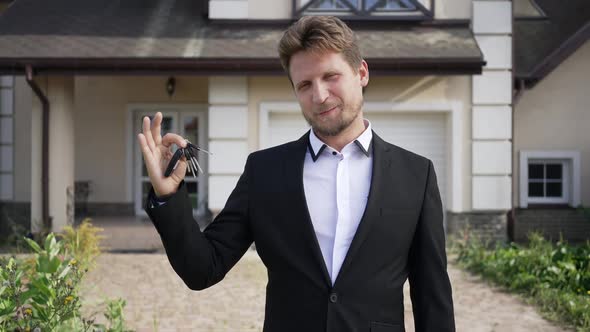 Portrait of Successful Smiling Businessman Boasting House Keys Standing in Sunshine Outdoors alt