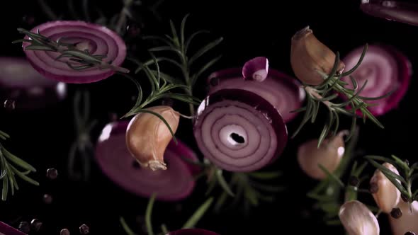 Slow Motion Flying Onion Rings and Garlic Cloves with Rosemary and Spices on a Black Background alt