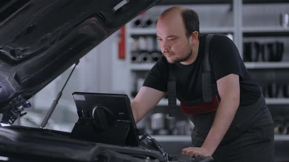 Male Mechanic Uses a Tablet Computer with an Augmented Reality Diagnostics Software alt