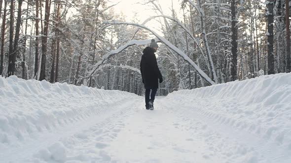 young man in warm winter clothes walks through the winter snow forest. alt