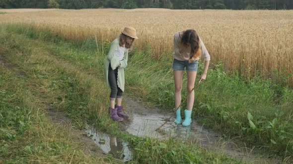 Two Happy Girls Sisters in Boots Playing in Puddle of Rainwater alt